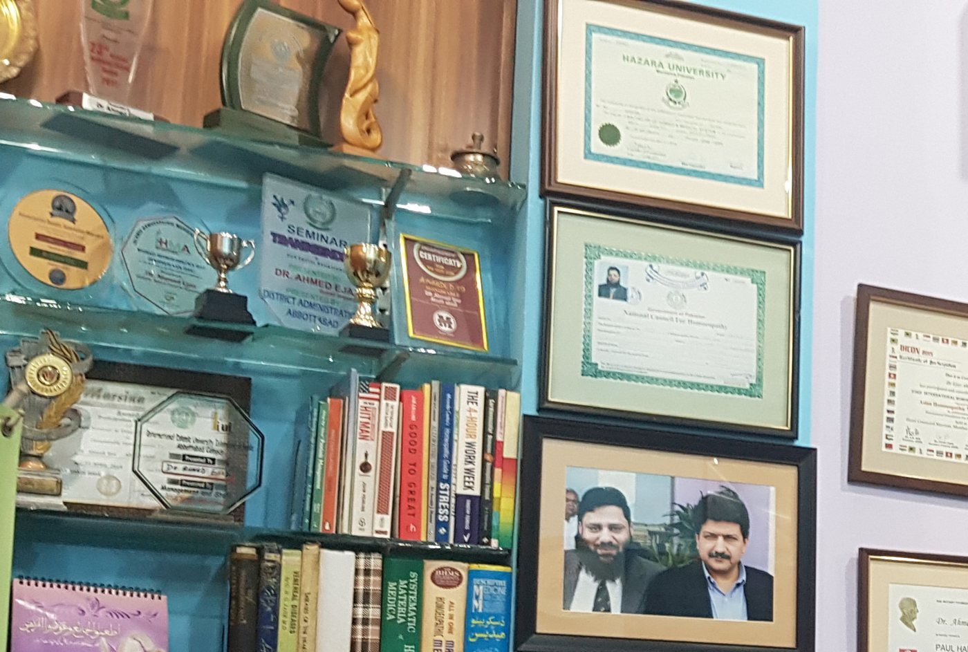 A private consultation room with framed certificates, books and an examination couch